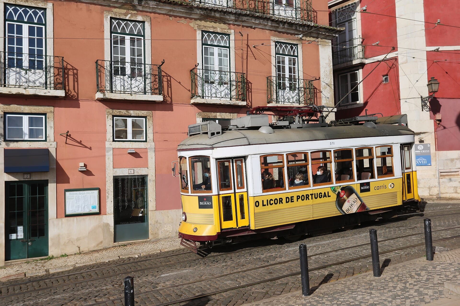 A yellow tram passing pink houses in Alfama, Lisbon